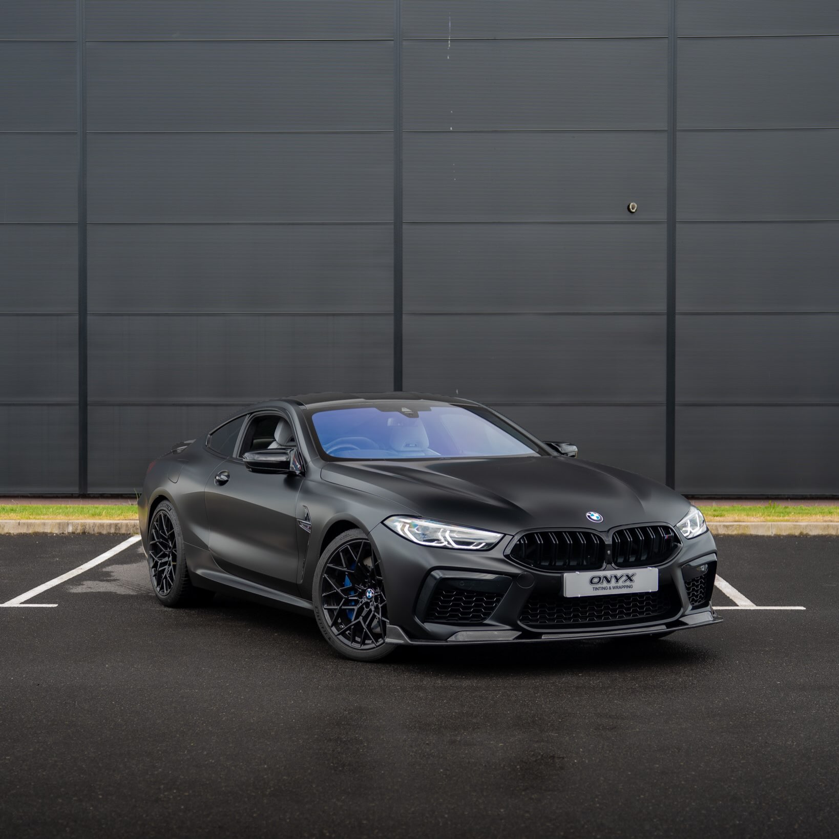 BMW M8 Competition F92 coupé with a satin black HEXIS wrap, viewed from the front three-quarter angle